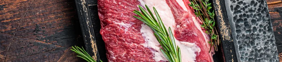Close up shot of raw meat with herbs beside a metal knife