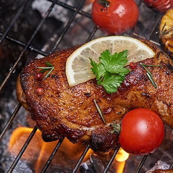 Chicken with herbs and spices and vegetables being cooked on a grill smoker