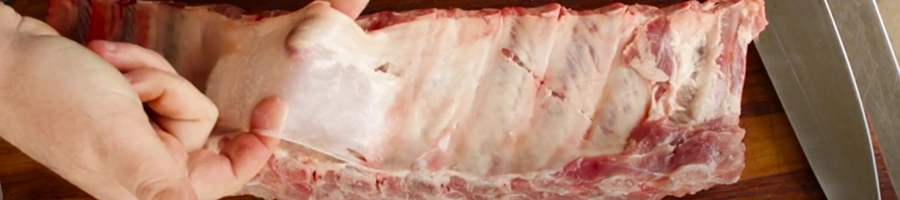 A hand pulling up the silverskin from the ribs