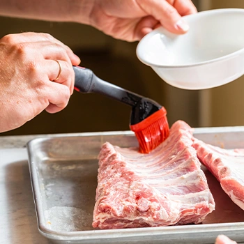 A hand with brush marinating the meat ribs