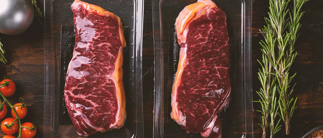 Two raw vacuum sealed meat on a table with herbs on the side