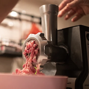 A close up image of a meat grinder used by a man
