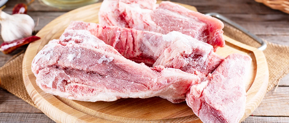 A close up image of frozen meat on top of a wooden board
