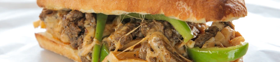 A close up image of a Philly cheesesteak sandwich on top of a paper