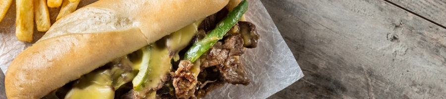 A top view image of a Philly cheesesteak sandwich with a side of fries