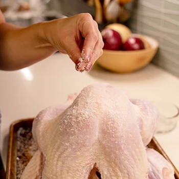 A woman seasoning to cook a turkey with kosher salt