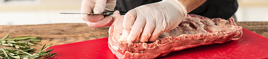 A chef trimming a piece of meat on a cutting board