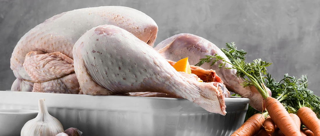 A raw chicken on a white plate with carrots on the side