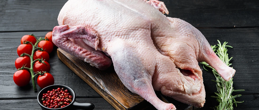 Raw whole duck meat on a wooden board with spices on the side