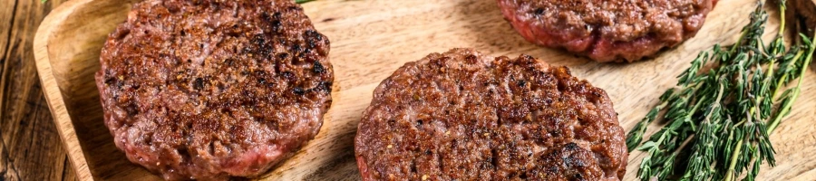 Cooked hamburgers sitting out on a wooden plate