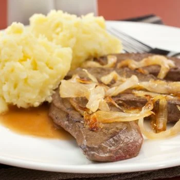 A perfectly cooked steak on a white plate with sides