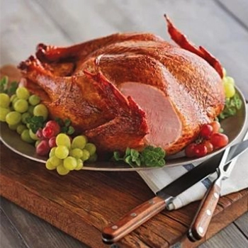 Roasted Chicken on a metal plate that is on a wooden board with grapes and utensils on the side