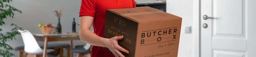 Man in red shirt holding ButcherBox food delivery package recently arrived inside his house