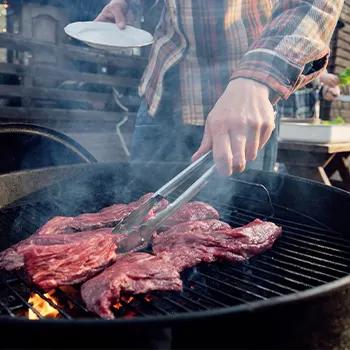 Man using a thong while grilling raw meat outdoors