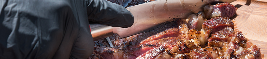 A hand with gloves cutting brisket meat