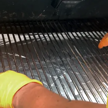A person cleaning the inside of a pellet grill