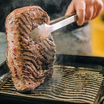 Cooking meat on an electric countertop grill and holding the meat with tongs