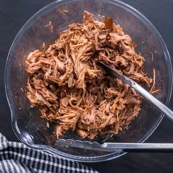 Cooked pulled pork in a bowl with thong