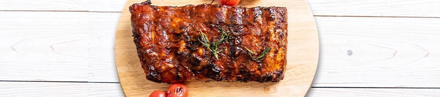 Freshly cooked ribs on circle cutting board above wooden platform