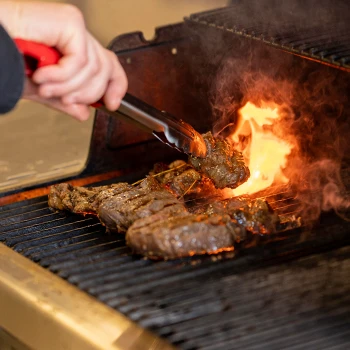 Grilling meat with small bright flame using tongs to hold the meat