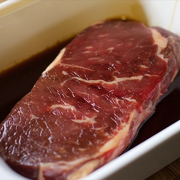 Sirloin steak being marinated inside a small white tray plate