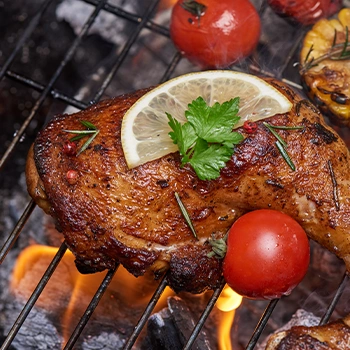 Close up image of grilling chicken with lemon slices and tomatoes