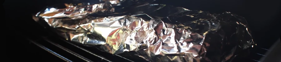 Baby back ribs covered in aluminum foil inside a smoker