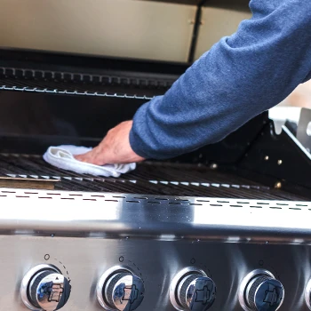 A person wiping the gas grill