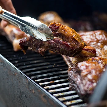 Using tongs to flip the meat inside the grill smoker