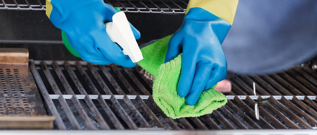 Spraying and wiping grill with protective gloves