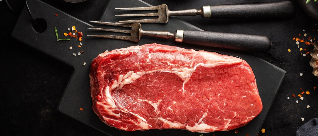 Top view of a raw meat on a black cutting board with forks