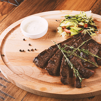 Skirt steak on a plate with vegetables and a dip