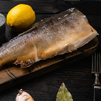 A dry smoked Trout fish on cutting board with lemon and fork
