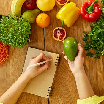 writing on a notebook while looking at green food