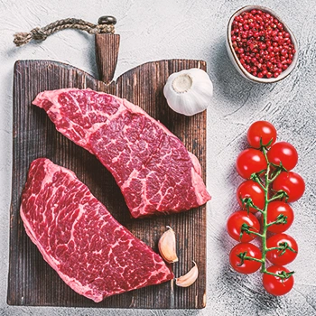 Raw meat on a chopping board with baby tomatoes