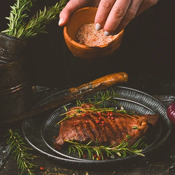 A person seasoning steak with salt