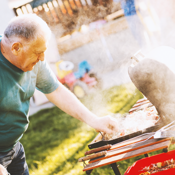 An old man checking out a grill in the backyard