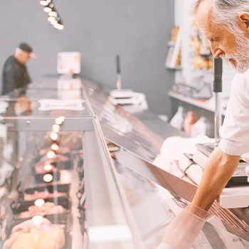 A butcher reaching in to a glass counter full of meat