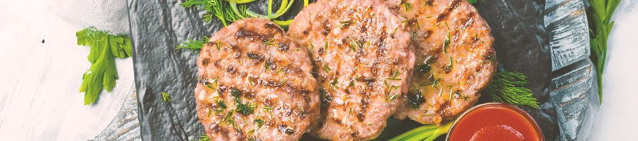 Grilled burger patties on a plate with leafy garnish