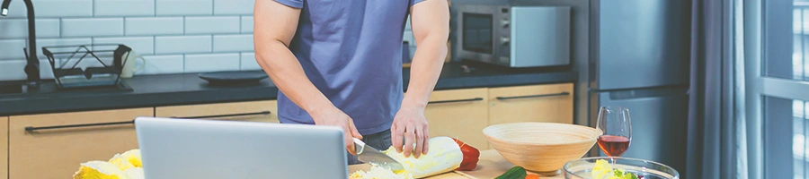 A buff person making food while looking at a laptop