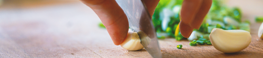 A person slicing garlic on a wooden board