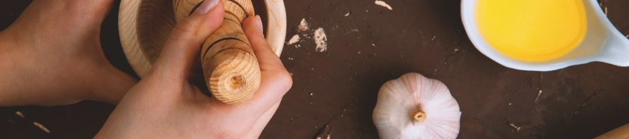 A person grinding garlic with butter oil on a porcelain spoon on the side