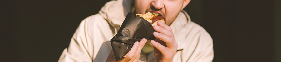 A person eating a sandwich holding it in a black paper wrapper