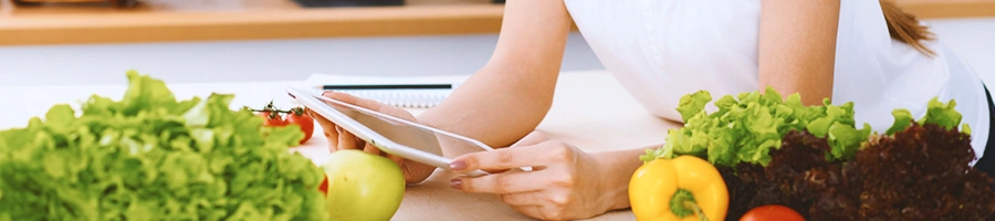 A person looking at a tablet with vegetables around