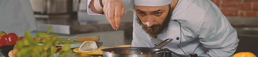 A chef cooking in a kitchen and adding seasoning to a pan