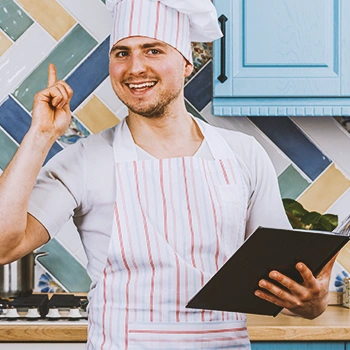 A chef holding a recipe and raising his finger
