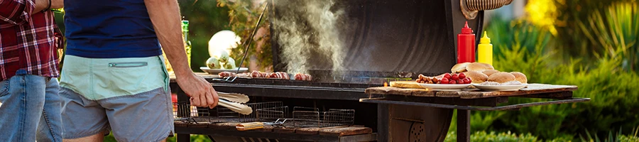 Two men cooking in front of a smoker grill