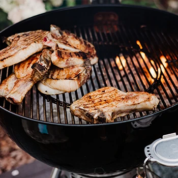 A close up image of a charcoal grill with meats on top