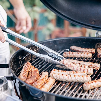 A person grilling sausages in a charcoal grill