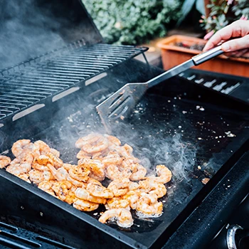 A person grilling shrimp at a smoker grill